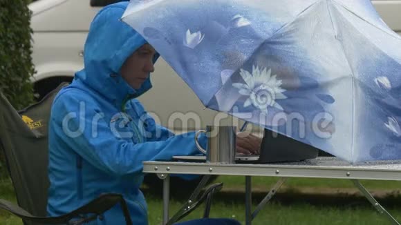 一个年轻的女人在雨中的蓝色伞下工作视频的预览图