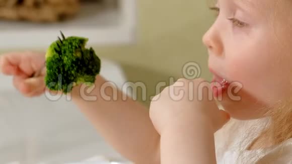 在家里的餐桌上一个漂亮的小女孩高兴地吃着西兰花和青豆视频的预览图