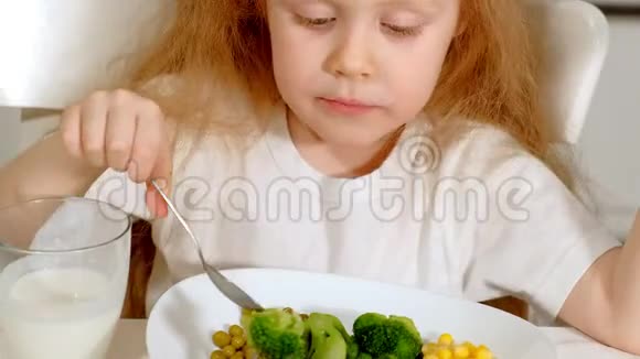 在家里的餐桌上一个漂亮的小女孩高兴地吃着西兰花和青豆视频的预览图