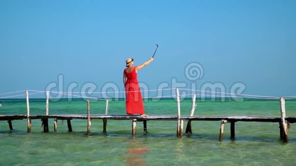 一位漂亮的女士用自拍棒上的动作相机拍摄自己的视频岛上阳光明媚普惠视频的预览图