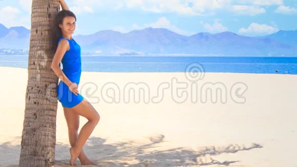 穿着蓝衣的女孩赤着脚斜靠在棕榈树干下视频的预览图