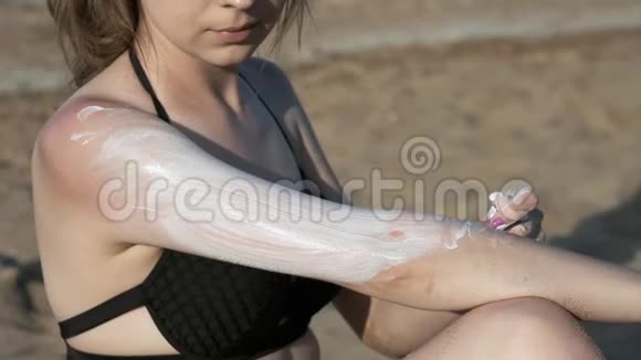 穿着黑色泳衣的海滩上的女孩涂了防晒霜或防晒霜在海边的沙滩上视频的预览图