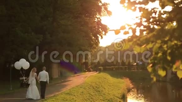 美丽的新婚夫妇带着气球在夕阳下的金秋公园散步视频的预览图