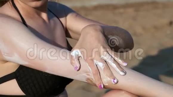 穿着黑色泳衣的海滩上的女孩涂了防晒霜或防晒霜在海边的沙滩上视频的预览图