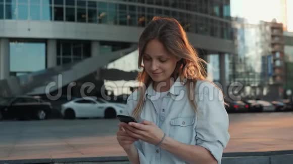 微笑女性使用智能手机语音识别的肖像年轻的白人女孩带着耳机走路视频的预览图