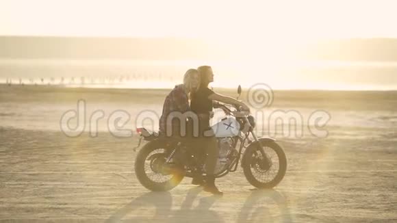 美丽的年轻女子摩托车手和他的女朋友骑摩托车在沙漠日落或日出骑自行车的女朋友视频的预览图