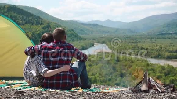 浪漫的旅游情侣在露营地拥抱在青山的岩石山顶上篝火视频的预览图