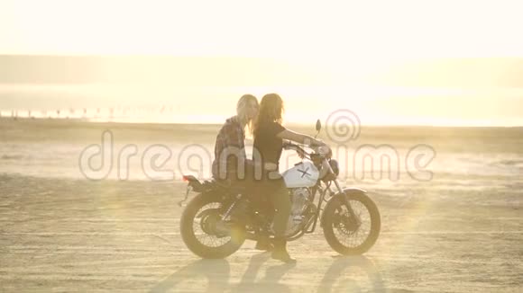 美丽的年轻女子摩托车手和他的女朋友骑摩托车在沙漠日落或日出骑自行车的女朋友视频的预览图