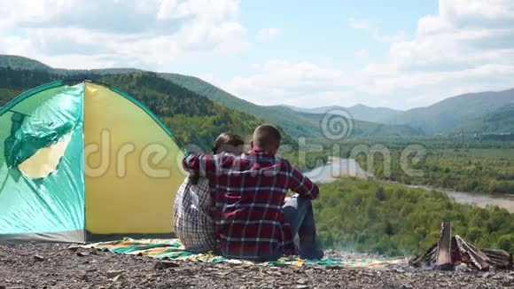 年轻的一对游客在绿山石顶的篝火旁拥抱营地视频的预览图