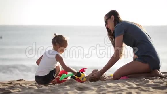 年轻的妈妈和小面包手在沙滩上玩沙子视频的预览图