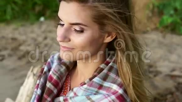 年轻漂亮的女孩坐在河边的一块格子布上享受日落视频的预览图