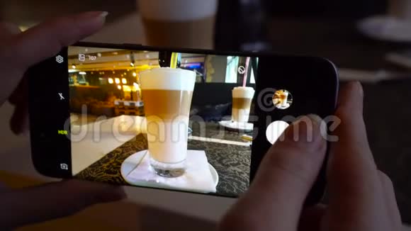 女孩在一家咖啡馆里用智能手机拍拿铁的照片视频的预览图