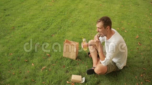 在草地上吃午饭的人男人在草坪上吃三明治喝果汁视频的预览图