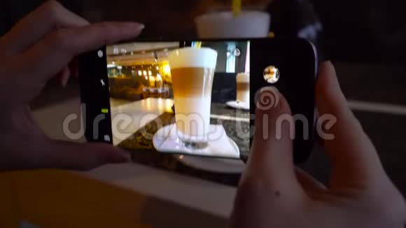 女孩在一家咖啡馆里用智能手机拍拿铁的照片视频的预览图