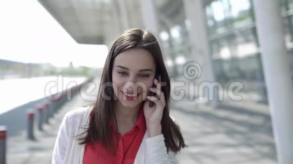 穿红衬衫的女人拿着手提箱在电话里说话视频的预览图