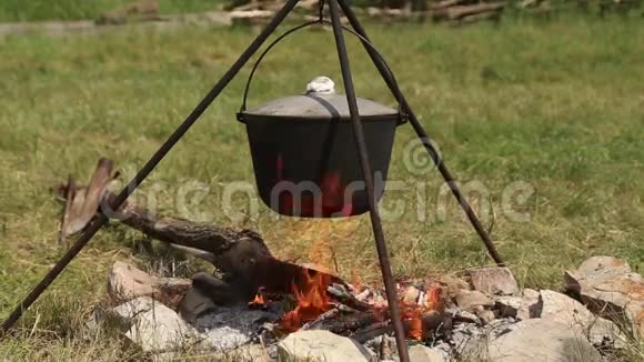 三脚架上的大锅在篝火上加热视频的预览图