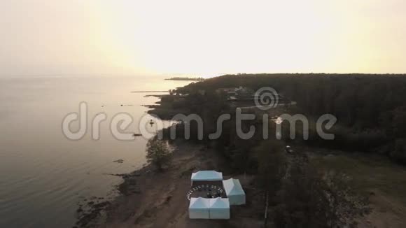 日落时在森林中的沙海海岸有白色帐篷和运动场视频的预览图