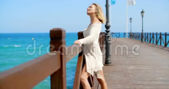 穿白色外套的金发女人站在码头上视频的预览图