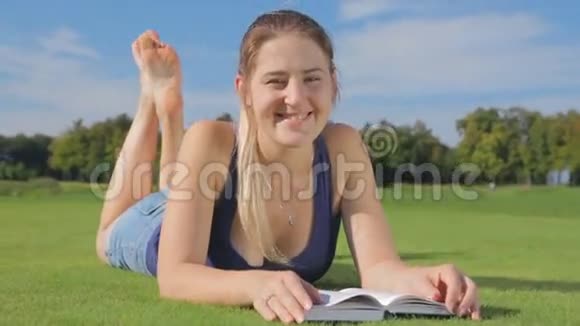 在公园的草地上躺着一本书的多莉微笑的年轻女孩视频的预览图