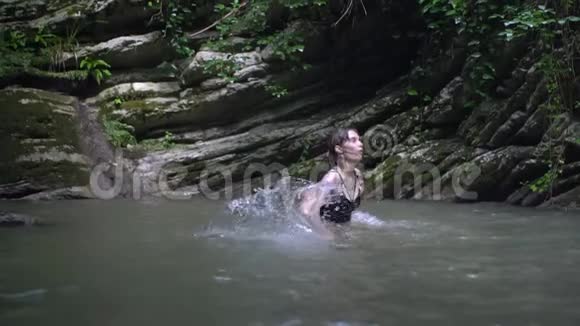 在绿色热带森林中的小山湖里年轻的美女双手泼水视频的预览图