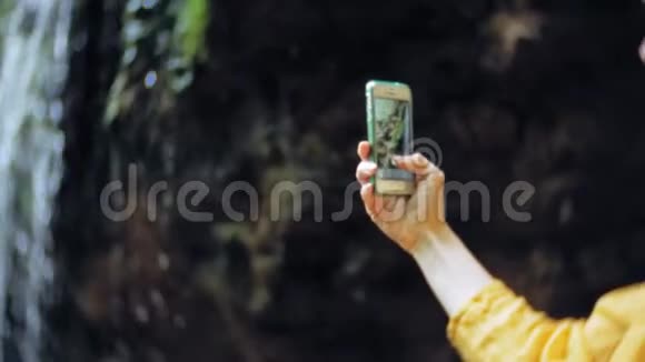 旅行冒险女在山上瀑布上拍摄智能手机欣赏大自然的美丽景色视频的预览图