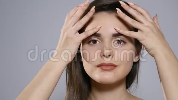 一位深褐色头发的漂亮女孩的特写镜头透过镜头在灰色的摄影棚墙壁背景上亲吻视频的预览图