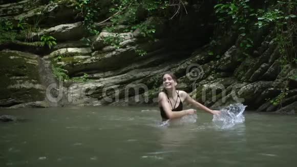 在绿色森林里的小山湖里年轻的美女双手泼水视频的预览图