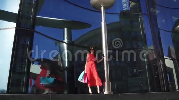 商店橱窗里漂亮的年轻女孩穿着红色裙子和太阳镜的黑发女人拿着购物袋视频的预览图
