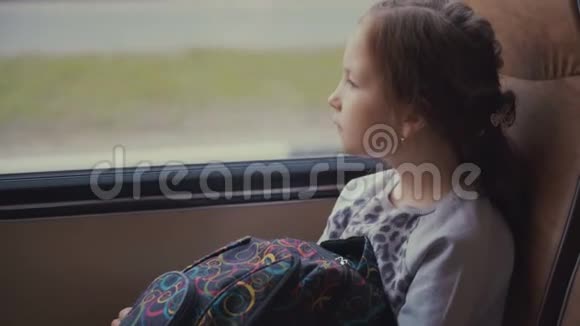 年轻美丽的女孩乘客拿着书包在移动的校车上看着窗外视频的预览图