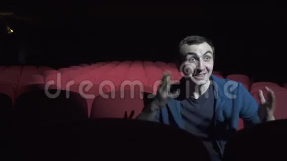 男人坐在黑暗的电影院里舒适的红椅子上看喜剧笑视频的预览图