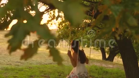 在公园日落时孩子们骑着一根绳子在橡树摇摆特写镜头女孩笑高兴年轻的女孩在荡秋千视频的预览图