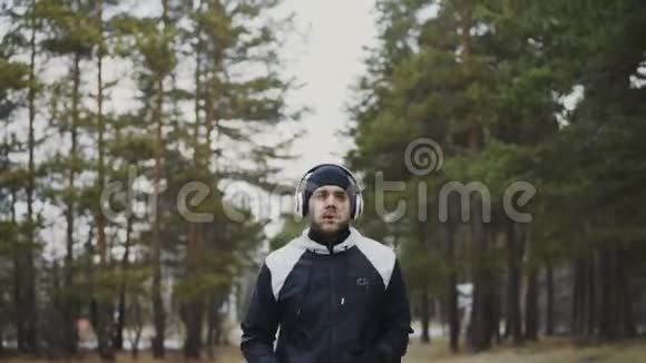 冬季公园早上听音乐时戴着耳机慢跑的跑步运动员视频的预览图