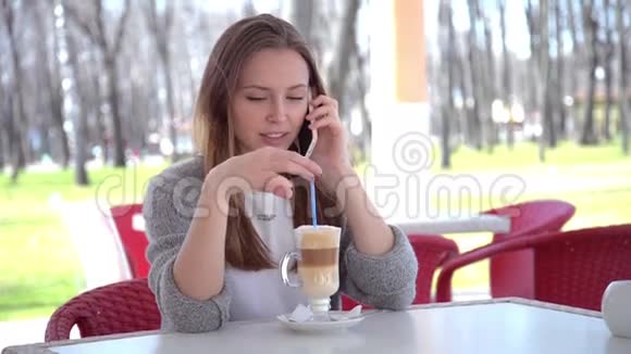 女人在智能手机上说话喝着咖啡在咖啡馆里笑美丽美丽视频的预览图