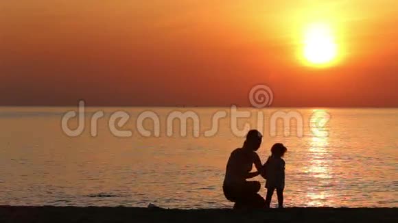 日出时在海滩上拥抱母女的剪影视频的预览图