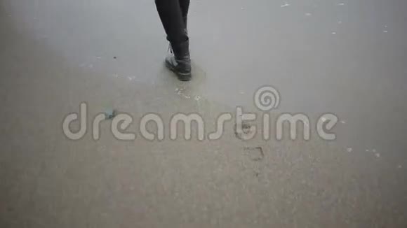 暴风雨时穿着粉红色外套的快乐女孩在海边大海在沙滩上冲刷着脚印视频的预览图