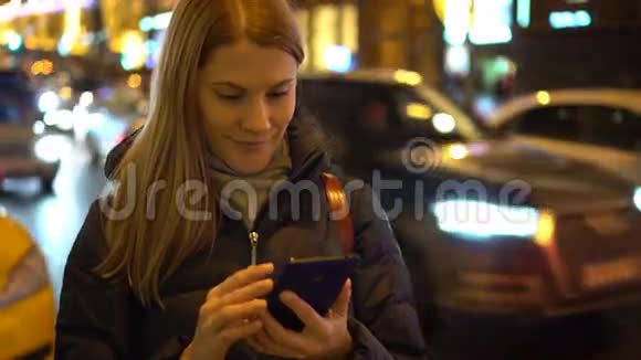 美丽迷人的年轻女人站在街上用她的智能手机城市灯光视频的预览图