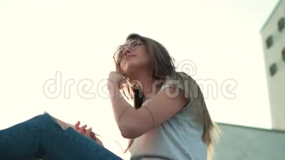 戴眼镜的布鲁内特女孩坐在夕阳下听音乐视频的预览图