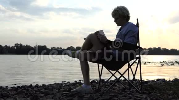 短裤中的年轻人在夕阳下的河岸上写了一些东西视频的预览图