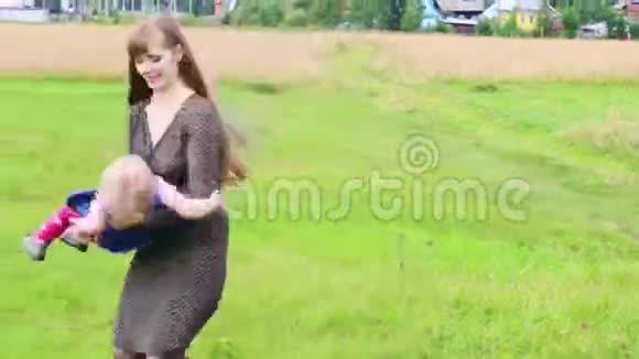 快乐的母亲在绿色的草地上旋转着小女儿视频的预览图