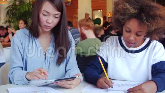 两个快乐的女孩亚裔和黑人在咖啡馆里聊天和工作视频的预览图