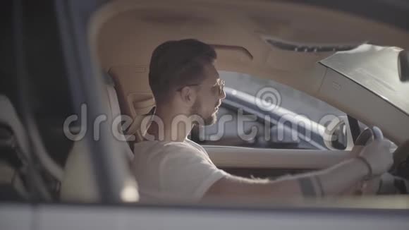 漂亮的年轻纹身男戴着太阳镜坐在豪华跑车对面准备开始比赛视频的预览图