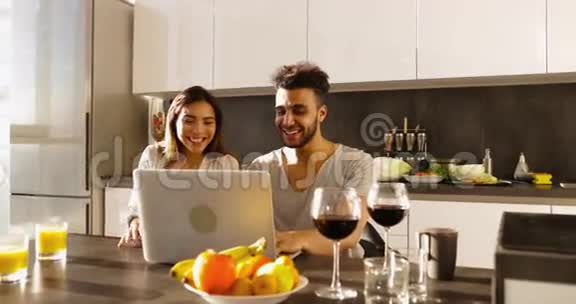 年轻混合种族夫妇使用笔记本电脑晨曦快乐西班牙男人亚洲女人一起在厨房视频的预览图