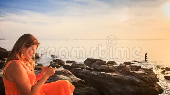 在日落时分用手机拍摄的海石上红色小女孩照片视频的预览图