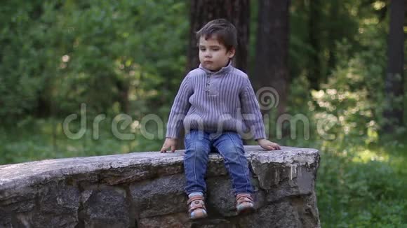 英俊的小男孩坐在石墙上思考视频的预览图