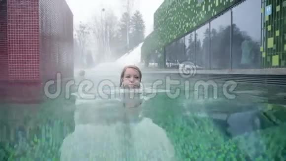 穿着蓝色比基尼的年轻女子在室外游泳池里向镜头游去视频的预览图
