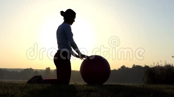性感的女人在夕阳下跪着滚她的健身球视频的预览图