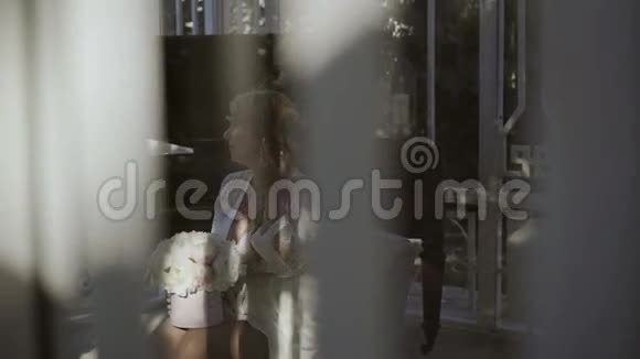 可爱的金发女郎穿着内衣坐在窗外的鲜花束中视频的预览图