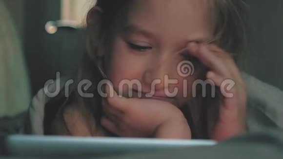在黑暗的光线下躺在床上的少女在社交网络上玩平板电脑特写小女孩看视频的画面视频的预览图