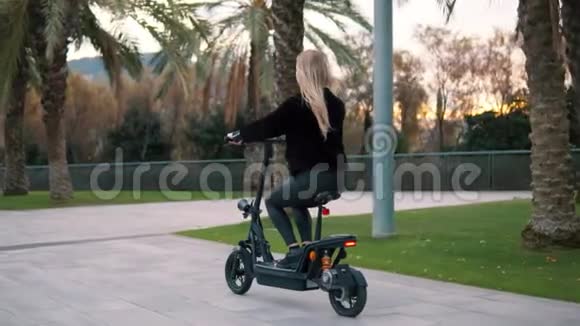 在城市公园驾驶电动自行车的金发美女视频的预览图