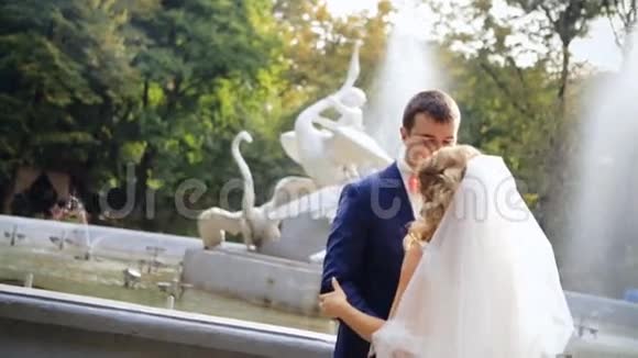 阳光明媚的一天年轻的新娘和新郎在喷泉附近视频的预览图